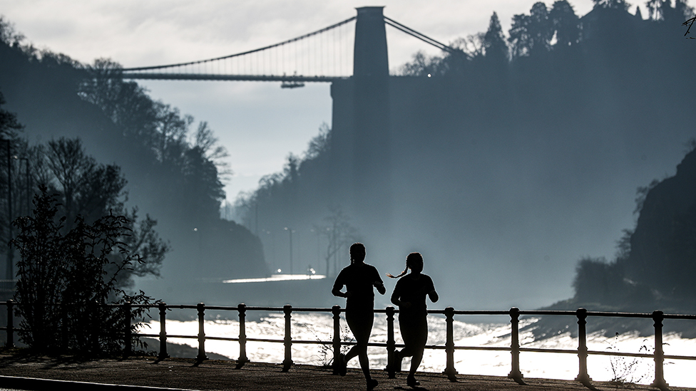 Joggers silhouetted against a background of Clifton gorge and suspension bridge, Bristol