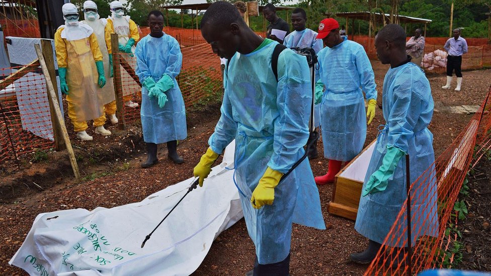 Sierra Leonese government burial team members disinfect the body bag